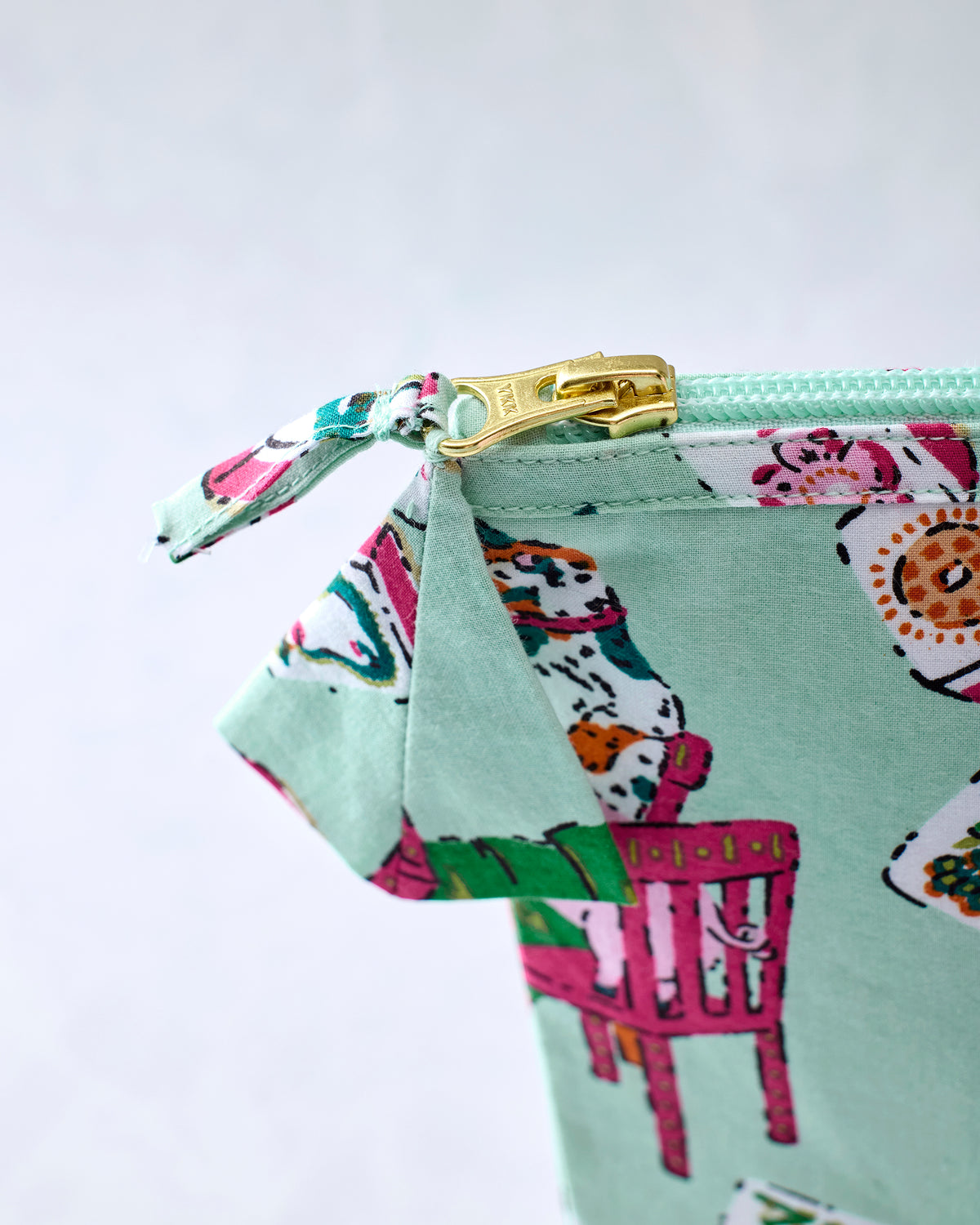 Close-up of the pale jade pouch showing its mint zipper, gold zipper pull, fabric tab, and printed tile scene.