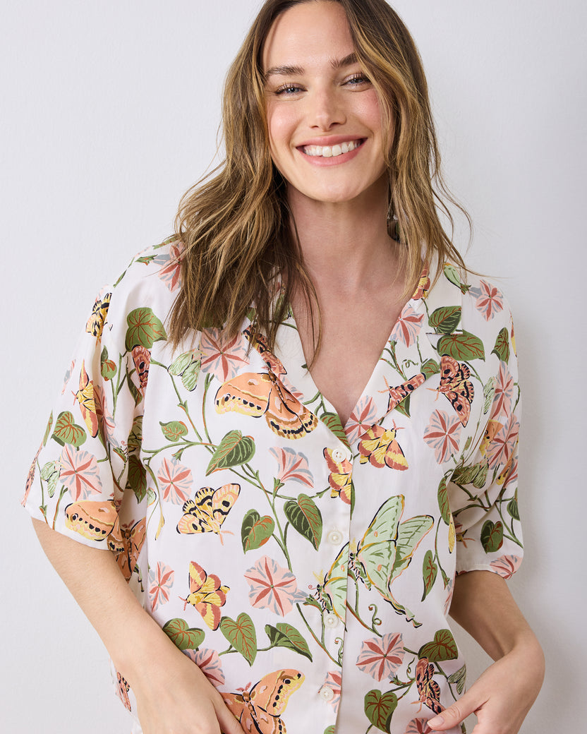 Close-up of an ivory button-front pajama top printed with moths, leaves, and pink flowers