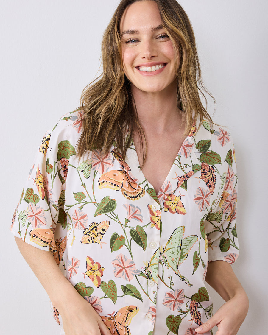 Close-up of an ivory button-front pajama top printed with moths, leaves, and pink flowers