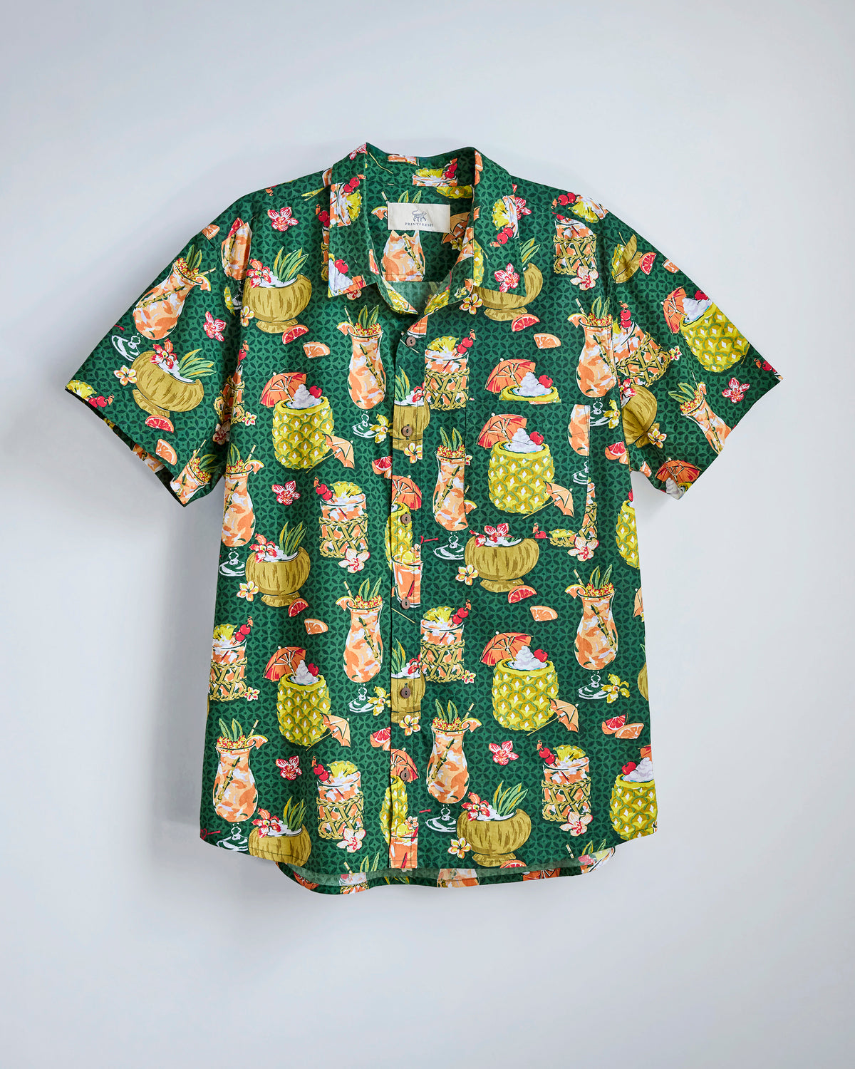 Flat-lay of the Emerald Isle Paradise Punch shirt with a tropical print of colorful drinks, pineapples, flowers, and umbrellas.