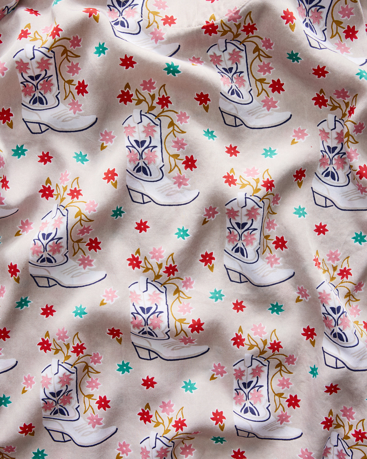 Close-up swatch of a light neutral print featuring repeated white Western boots filled with flowers and scattered colorful flowers.