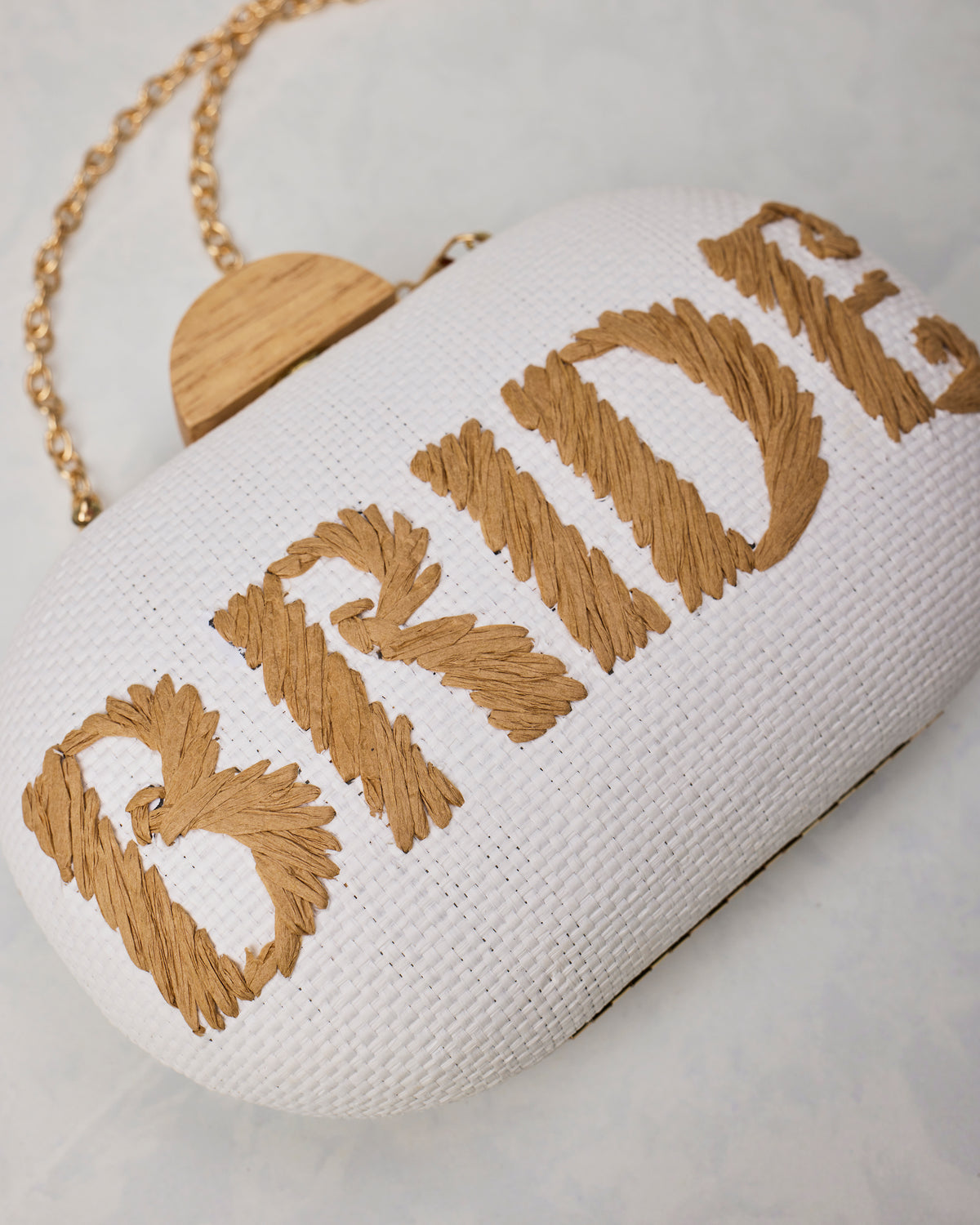 Close-up of the Bride clutch showing its white woven surface, tan embroidery, clasp, and gold chain.