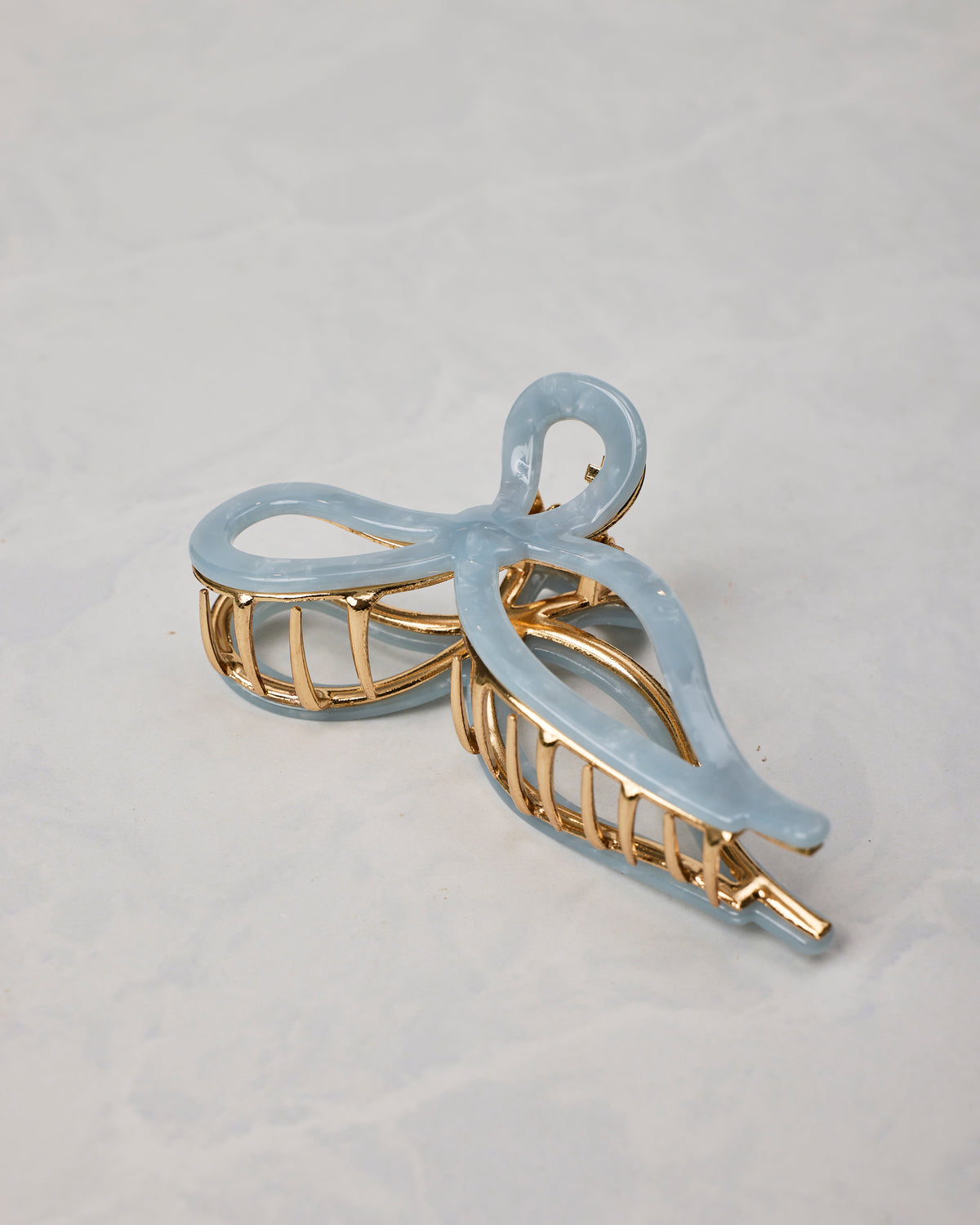 Pale blue ballet bow claw hair clip shown at an angle, with gold-toned teeth and frame.