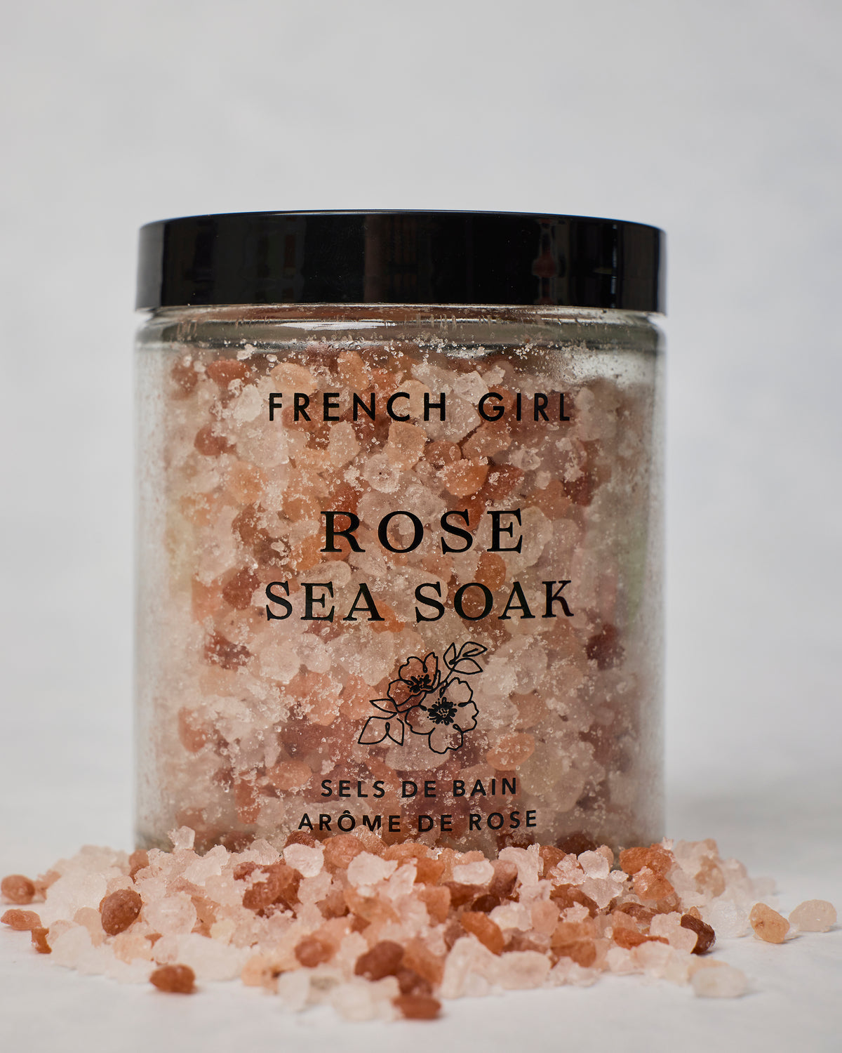 Jar of French Girl Rose Sea Soak bath salts with loose pink and white salts scattered in front.