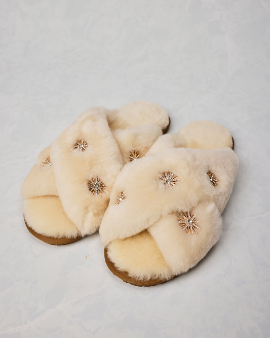 Pair of beige sheepskin slippers with gold-toned rhinestone starburst embellishments.