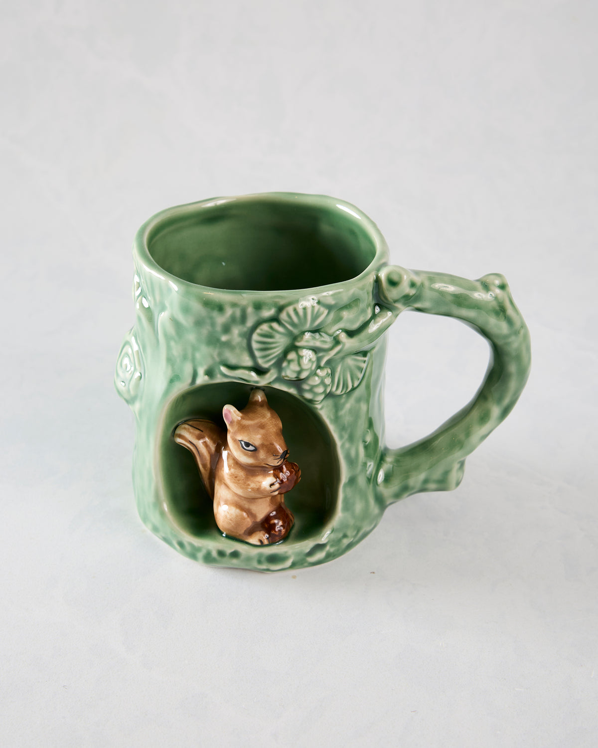 Green textured mug with raised woodland details, a handle, and a squirrel figurine in the front alcove.