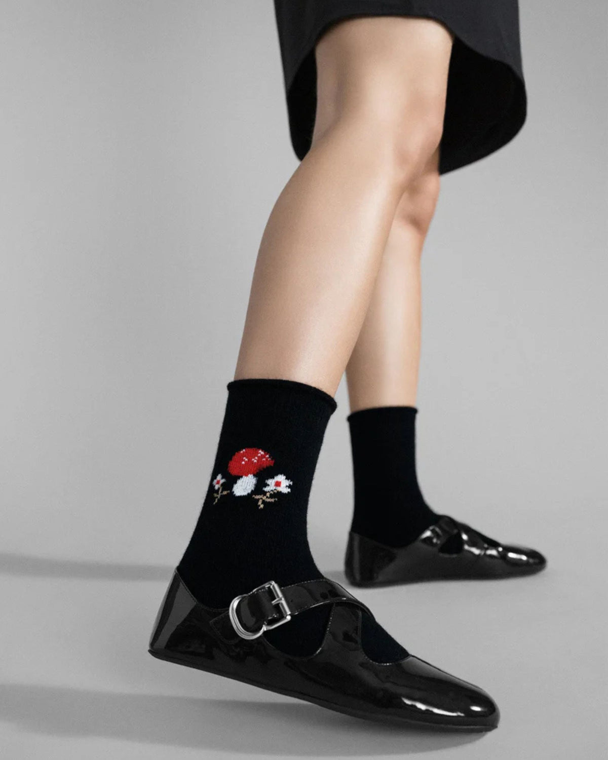 Black crew socks with embroidered red-and-white toadstool motifs, worn with glossy black buckle shoes.