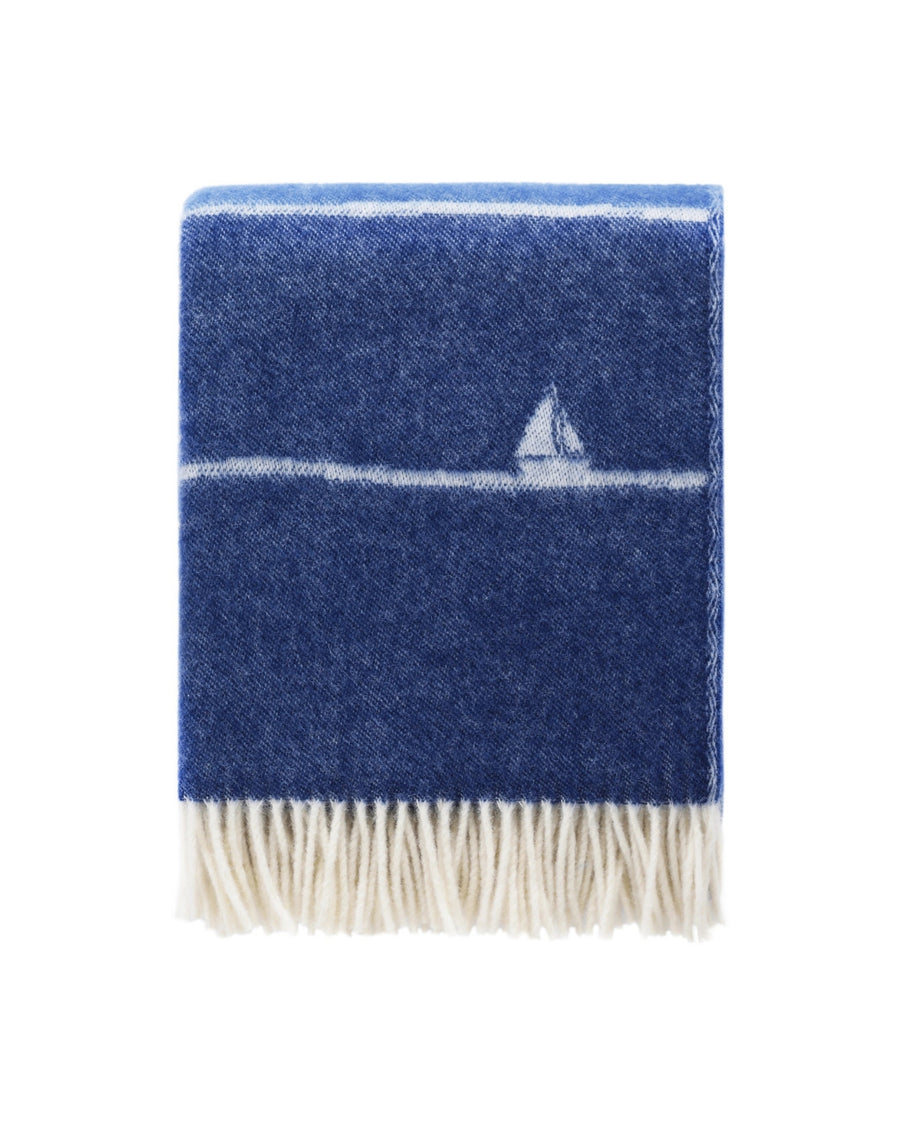 Boat wool throw folded to show a dark blue field, a white sailboat motif, and white fringe.