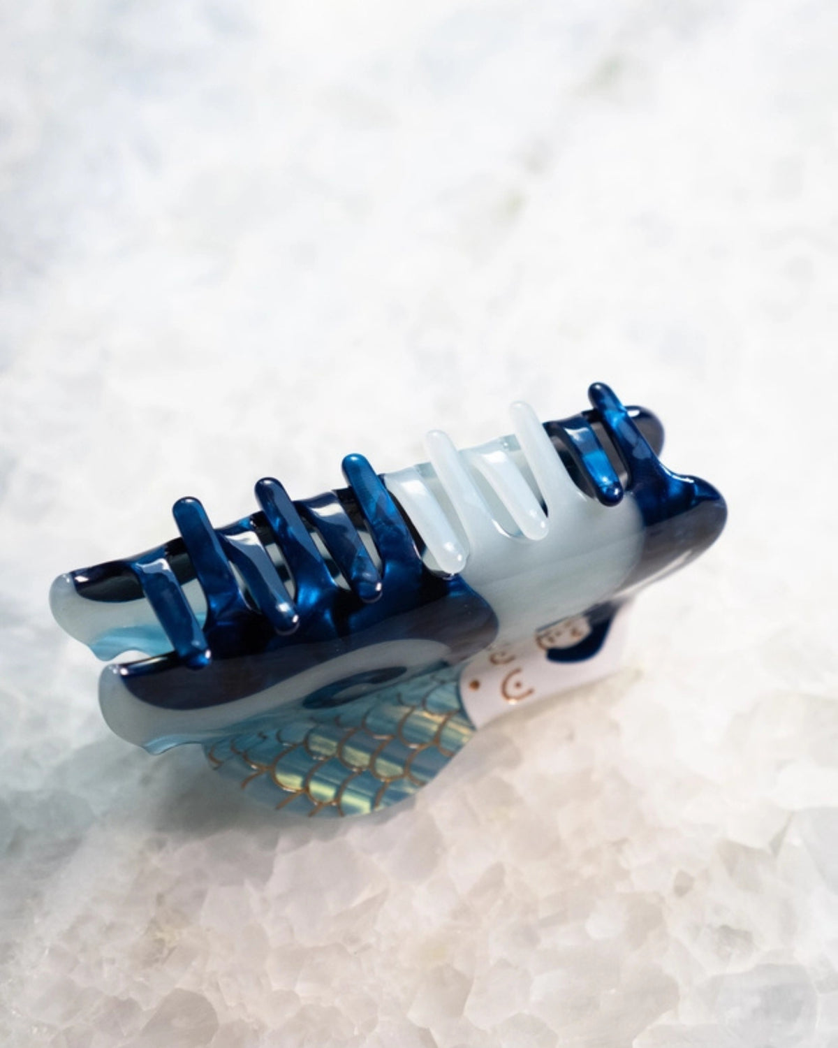 Underside view of the blue and white mermaid-shaped hair clip, showing its gripping teeth