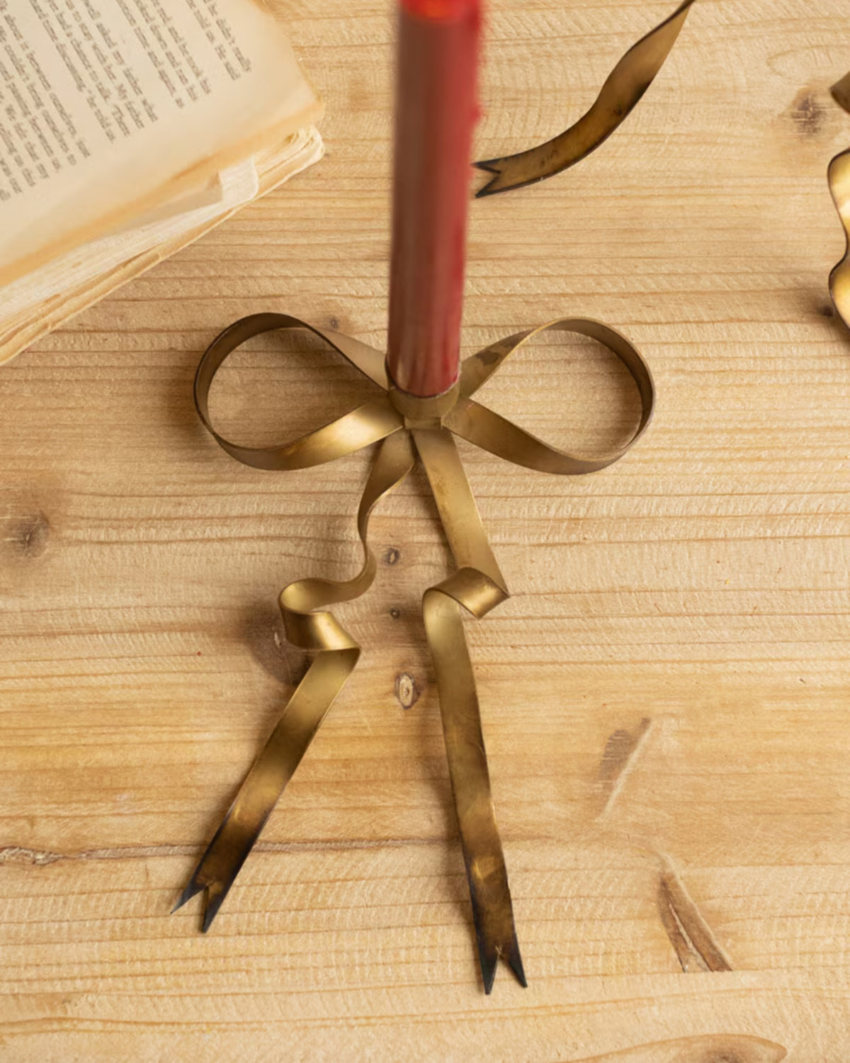 Close-up of an antique brass bow taper candle holder with a red taper candle
