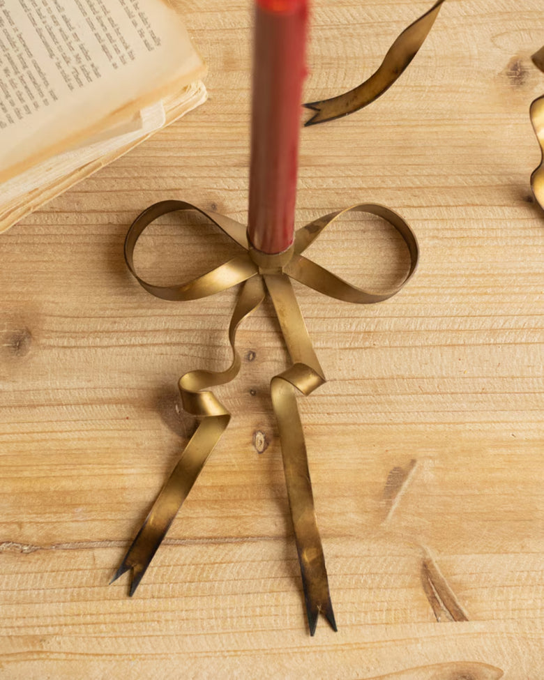 Close-up of an antique brass bow taper candle holder with a red taper candle
