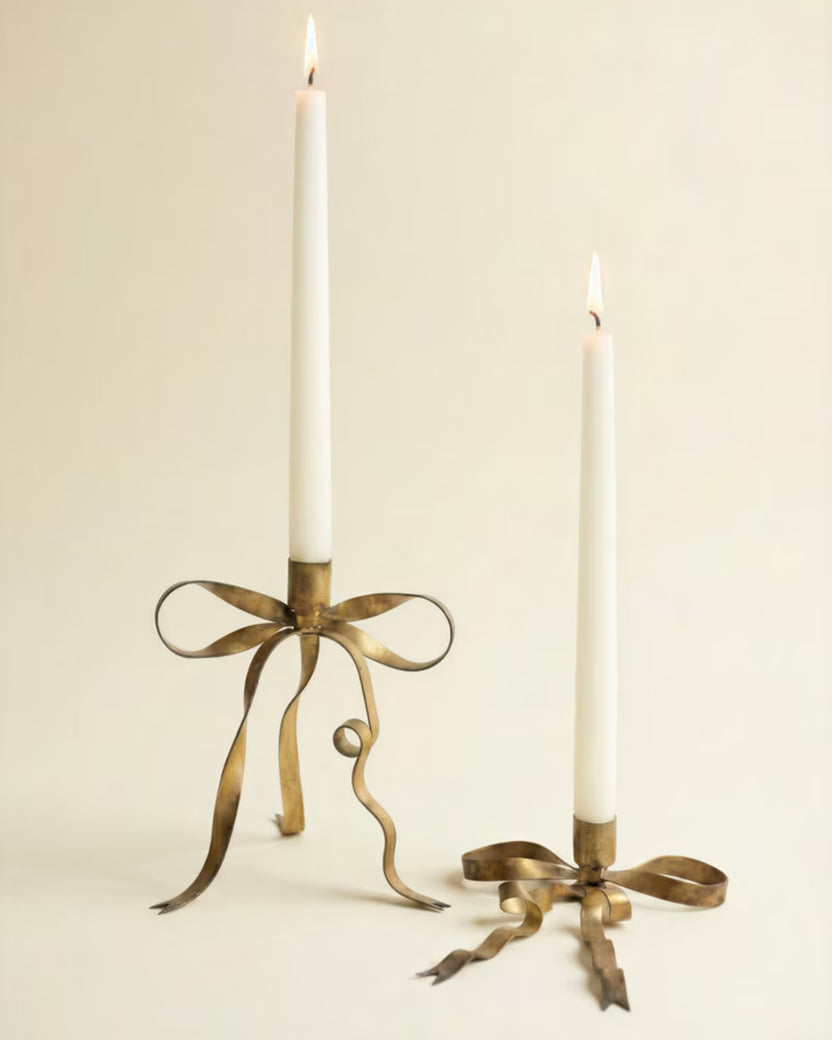 Two antique brass bow taper candle holders styled with white lit taper candles