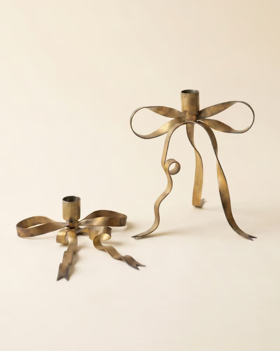Two empty antique brass bow taper candle holders shown together, with one raised behind the other