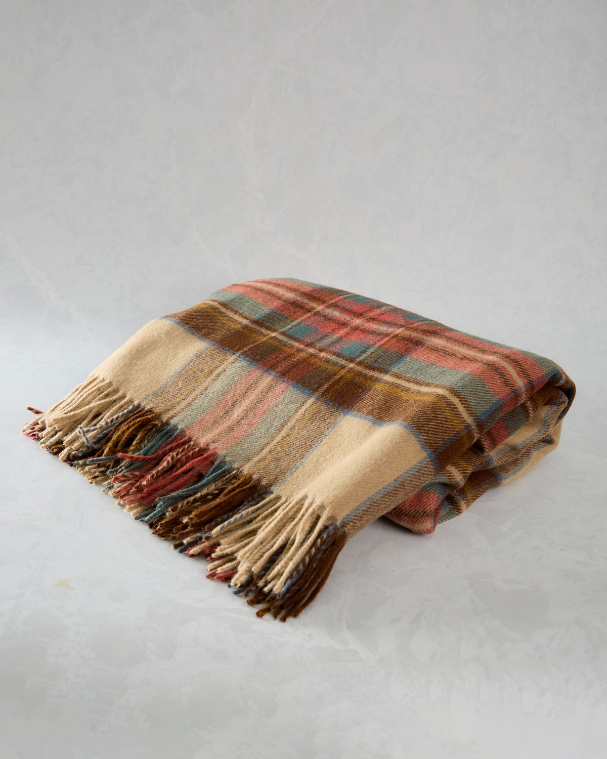 Camel plaid throw folded on a surface with multicolored stripes and fringed edges.