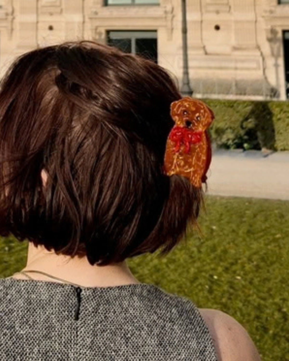 Brown puppy-shaped hair claw clip with a red bow, shown worn in short brown hair from the back.