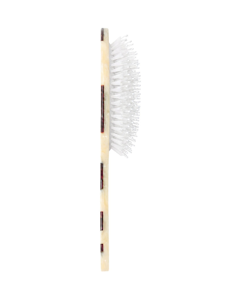 Side view of a hand-painted hair brush showing the depth of its white bristles and brown-and-cream handle.