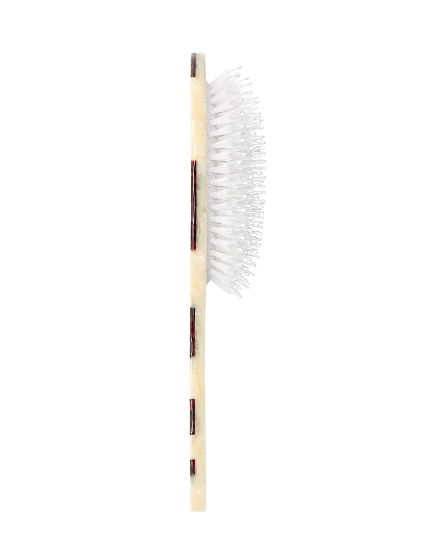 Side view of a hand-painted hair brush showing the depth of its white bristles and brown-and-cream handle.