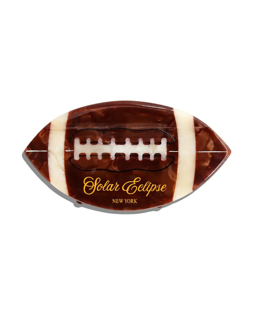 Front view of a brown football-shaped claw hair clip with white stripes and raised laces.