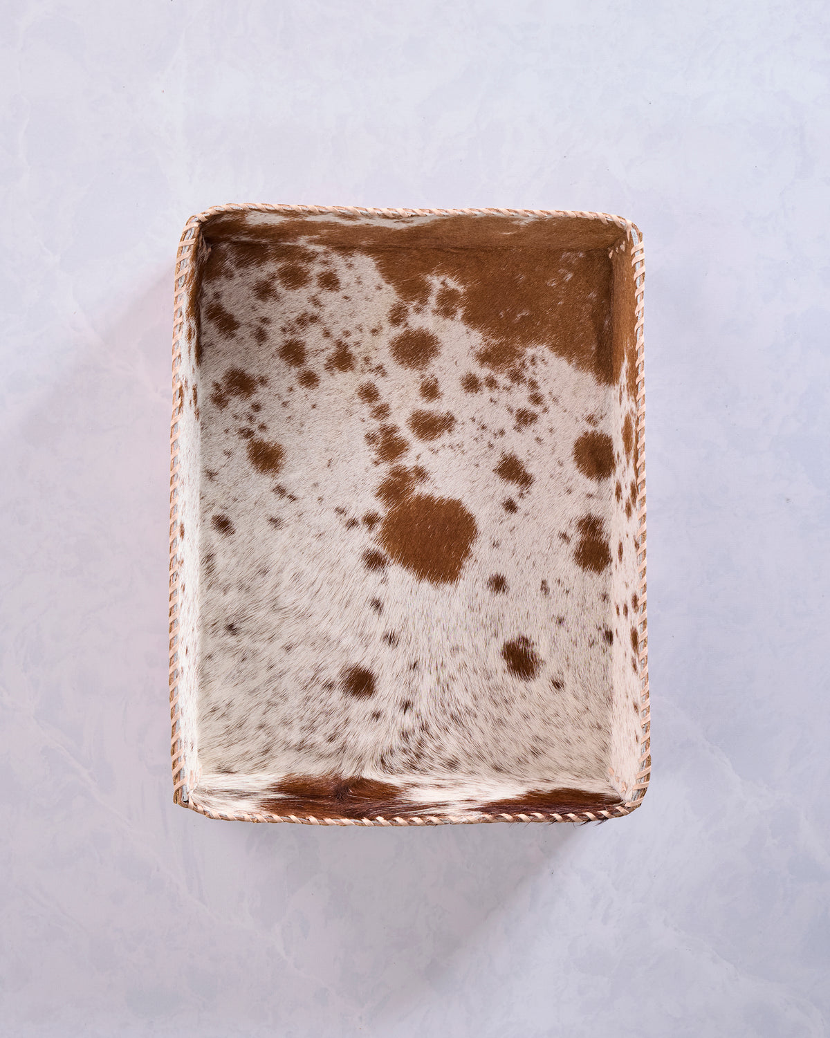 Top view of a rectangular brown cowhide leather tray with a spotted interior and stitched border.