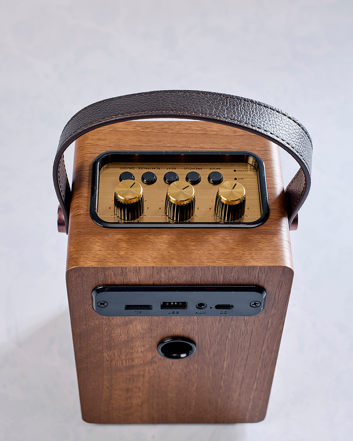 Rear view of the brown handled speaker showing its control panel, USB port, microSD slot, AUX input, and DC power input.