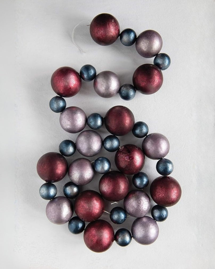 Christmas ball garland loosely coiled to show alternating burgundy, blue-gray, and mauve balls.