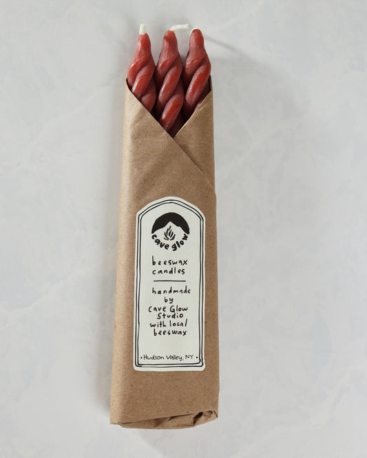 Packaged set of three red spiral candles in a brown paper sleeve with a Cave Glow Studio label.