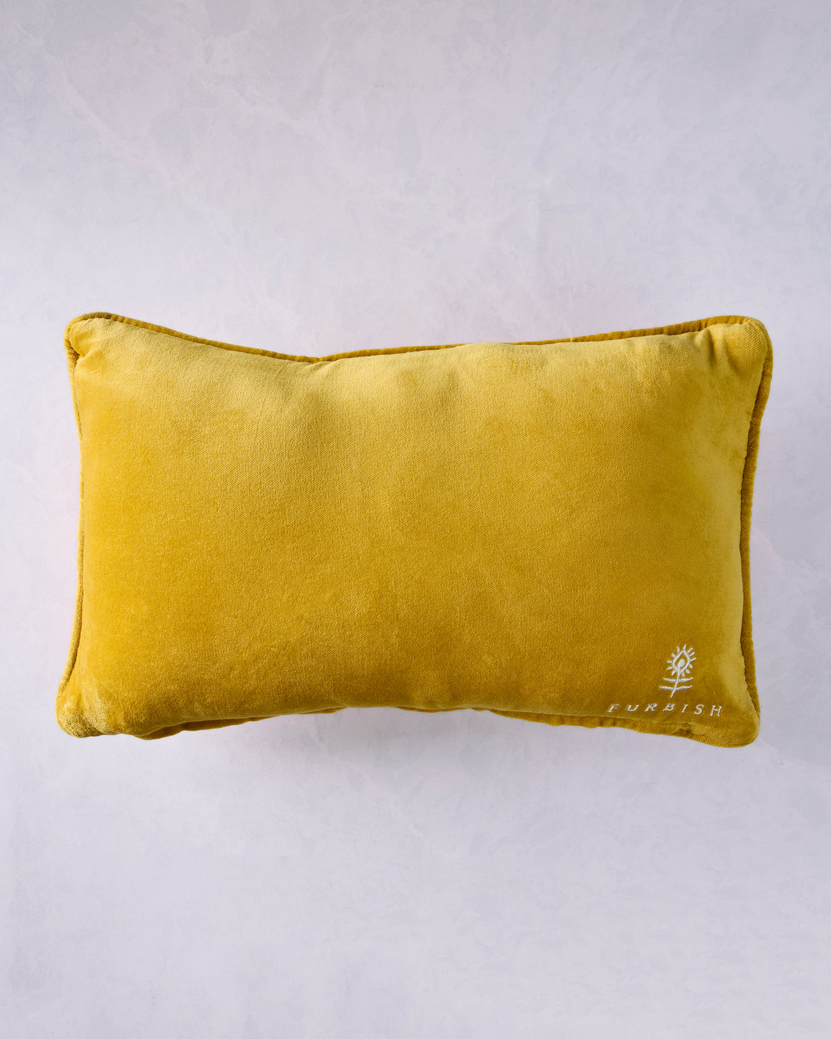 Back of a mustard-yellow pillow with a small white Furbish logo in the lower-right corner.