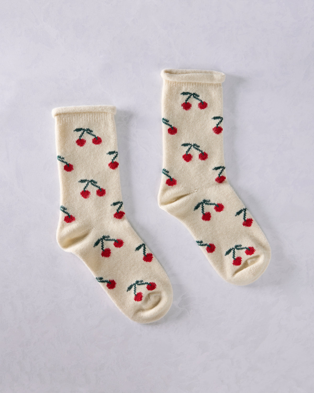 Pair of ivory crew socks with repeated red cherry and green stem motifs, shown from above.