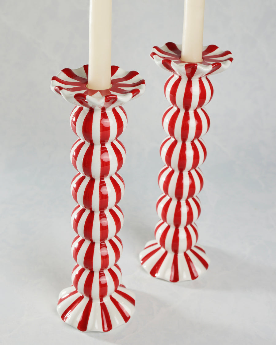 Close view of two red-and-white striped candle holders with ruffled candle cups and flared bases.