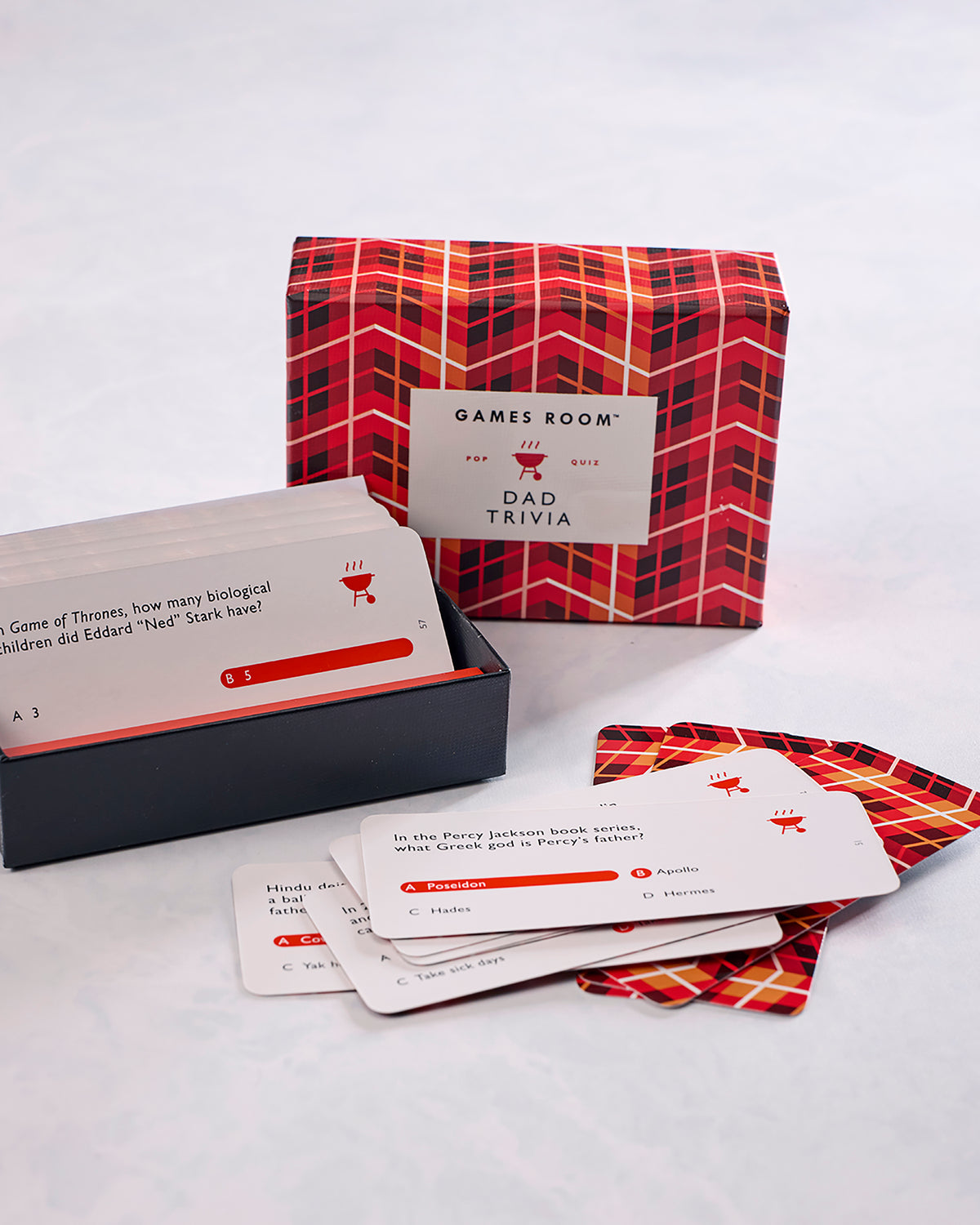 Dad Trivia card game shown in its red patterned box with question cards spread in front.