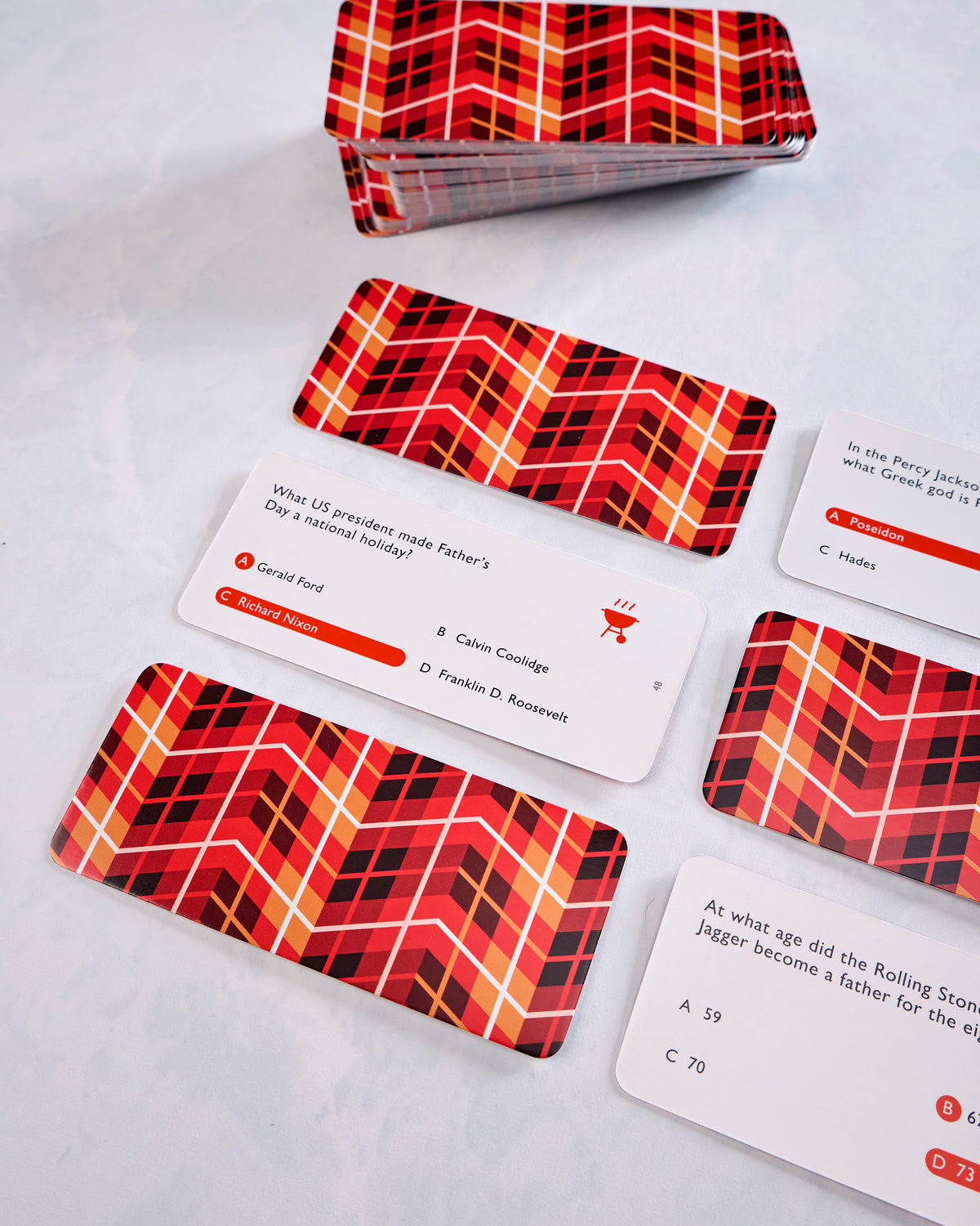Close-up of red patterned Dad Trivia cards, card backs, and the storage box, including multiple-choice question cards.