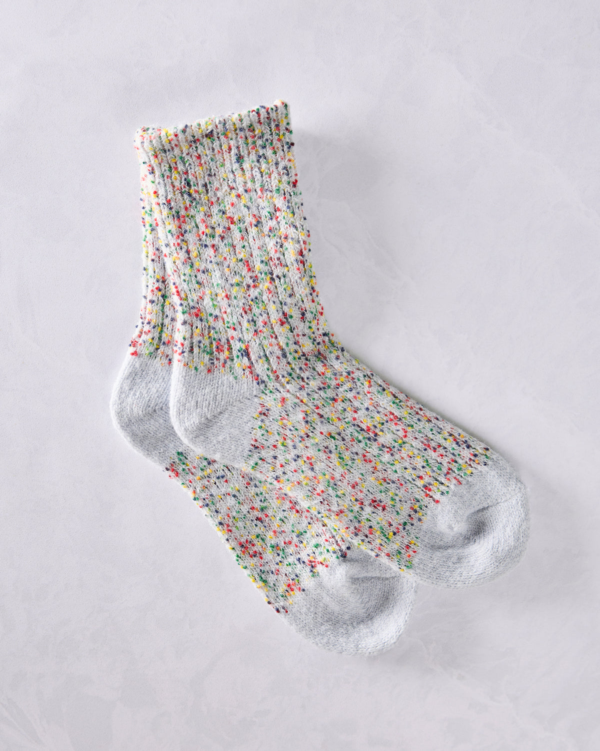 Pair of short crew socks with a light gray base and multicolored speckled knit pattern.