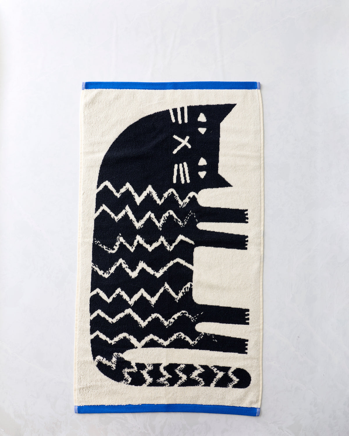 Black-and-cream hand towel with a large stylized cat design and blue edging, shown flat.
