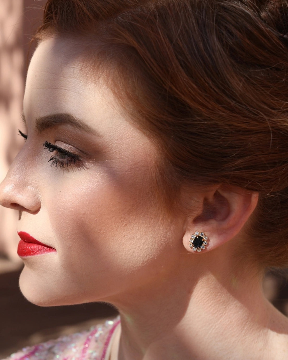 Side-profile view of a person wearing a rectangular dark green stud earring surrounded by clear stones.