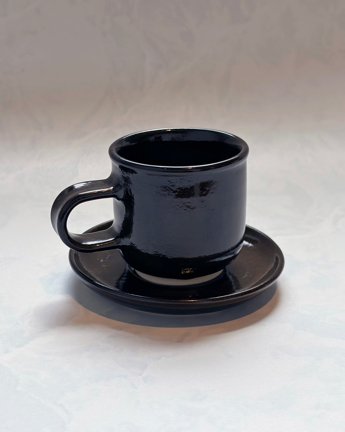 Black espresso cup resting on its matching saucer, shown from the front