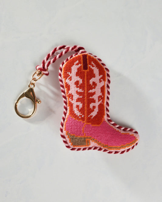 Close-up of a pink embroidered cowboy boot bag charm with a gold clip and twisted hanging loop.