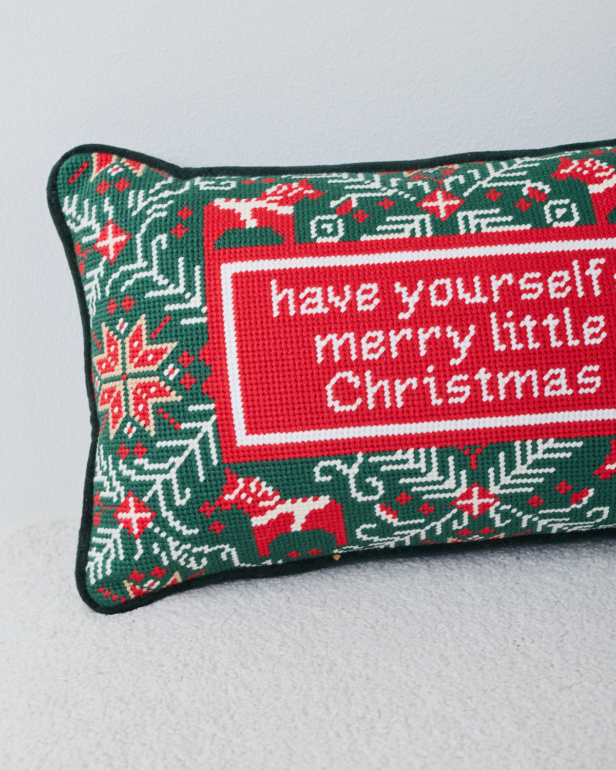 Close-up of the green needlepoint Christmas pillow showing the stitched holiday message, reindeer, and snowflake motifs.