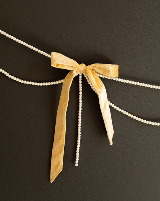 Gold velvet bow garland with faux pearl strands displayed against a dark background.