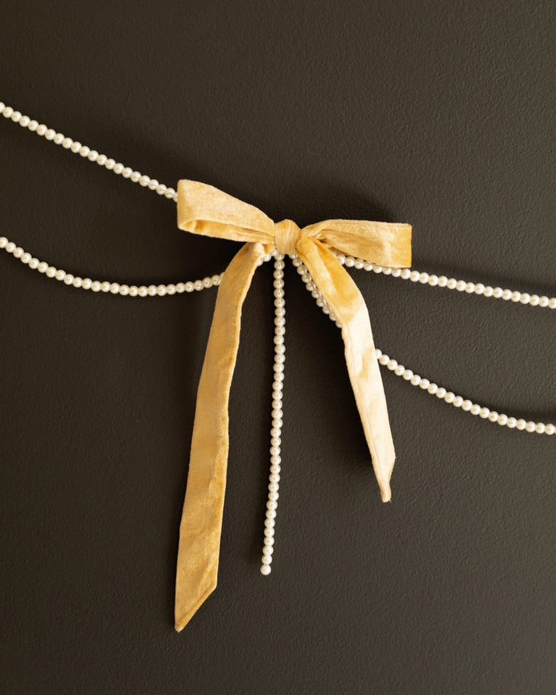 Gold velvet bow garland with faux pearl strands displayed against a dark background.