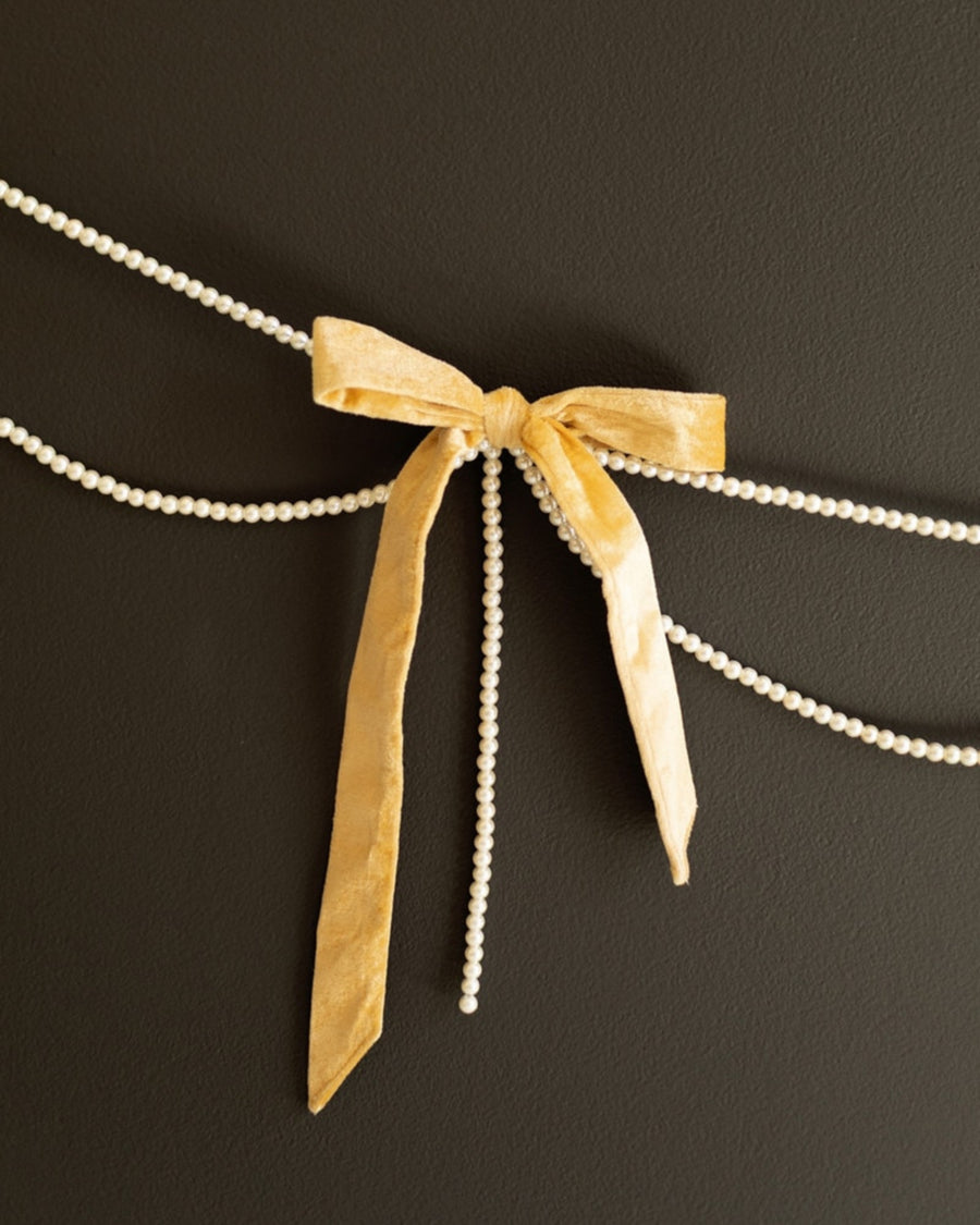 Gold velvet bow garland with faux pearl strands displayed against a dark background.