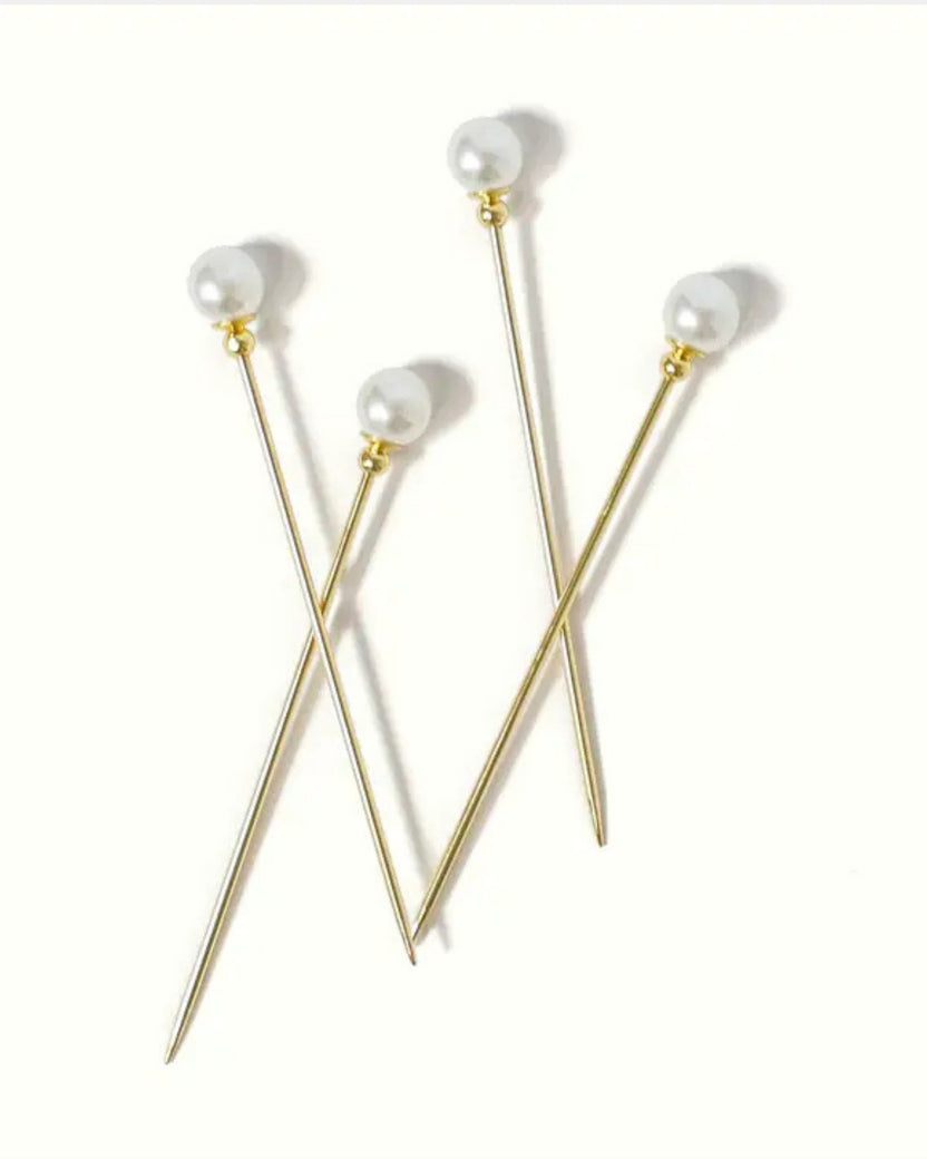 Four gold cocktail picks with white faux-pearl tops arranged on a white background.