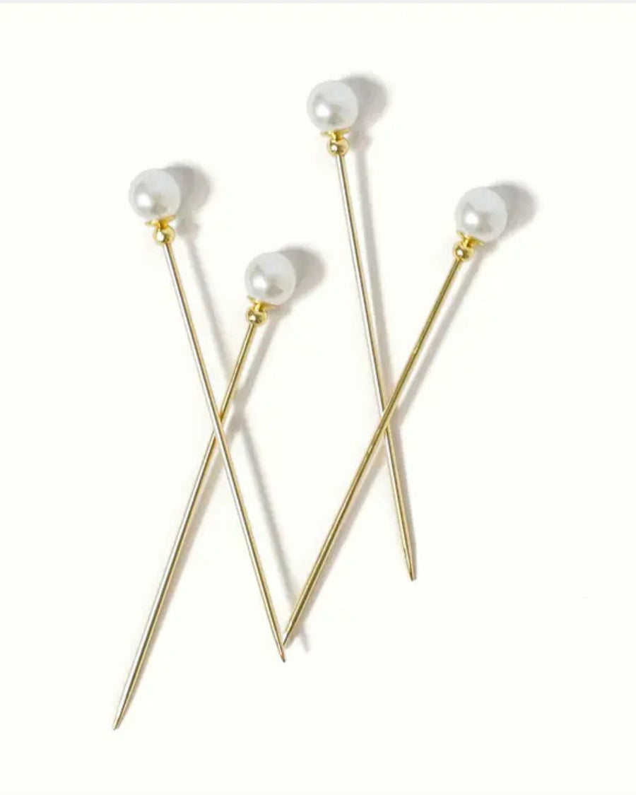 Four gold cocktail picks with white faux-pearl tops arranged on a white background.