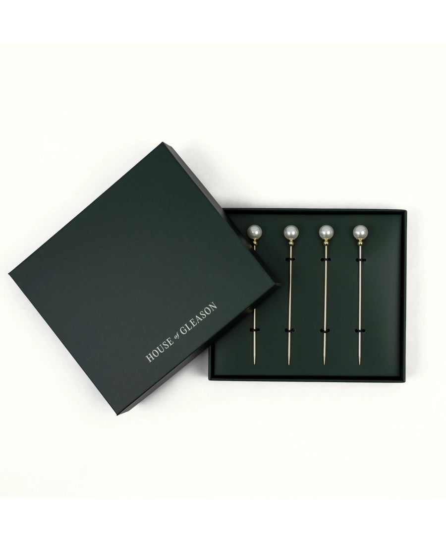 Four pearl cocktail picks displayed in a black presentation box beside its lid.