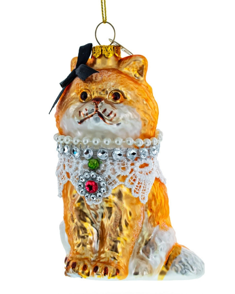 Front view of a seated orange cat glass ornament wearing a white lace collar with jeweled details and a black bow.