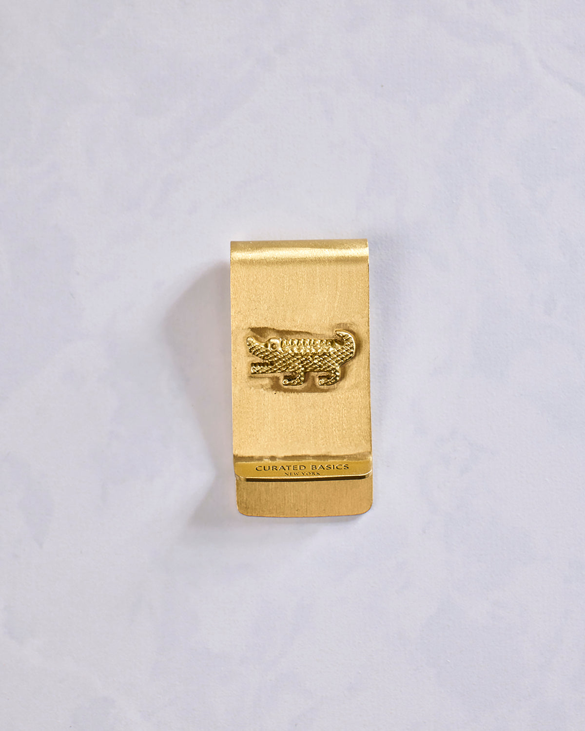 Front view of a gold crocodile money clip with a raised crocodile emblem and Curated Basics branding.