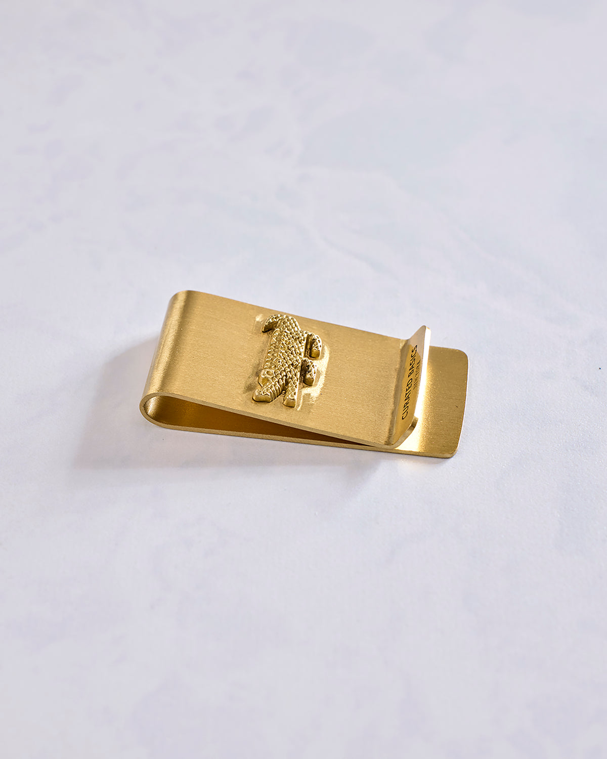 Angled view of a gold crocodile money clip showing its folded clip construction and raised crocodile emblem.