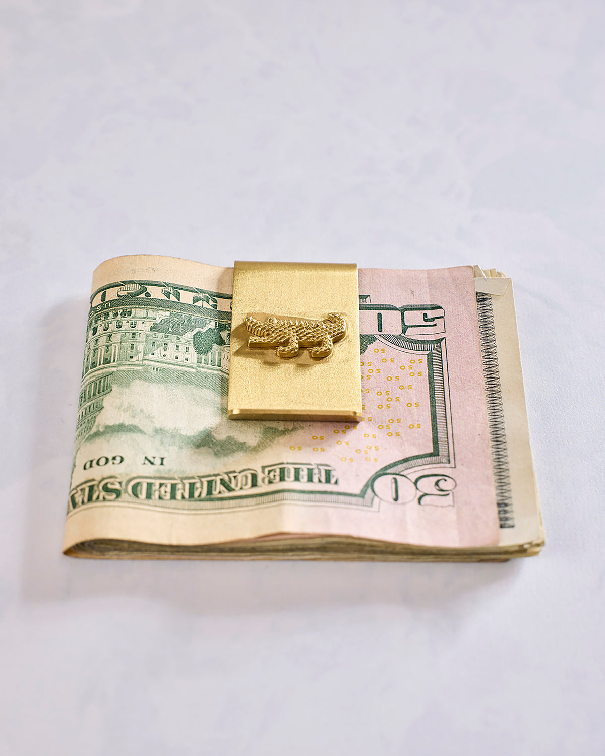 Gold crocodile money clip holding a folded stack of U.S. dollar bills.