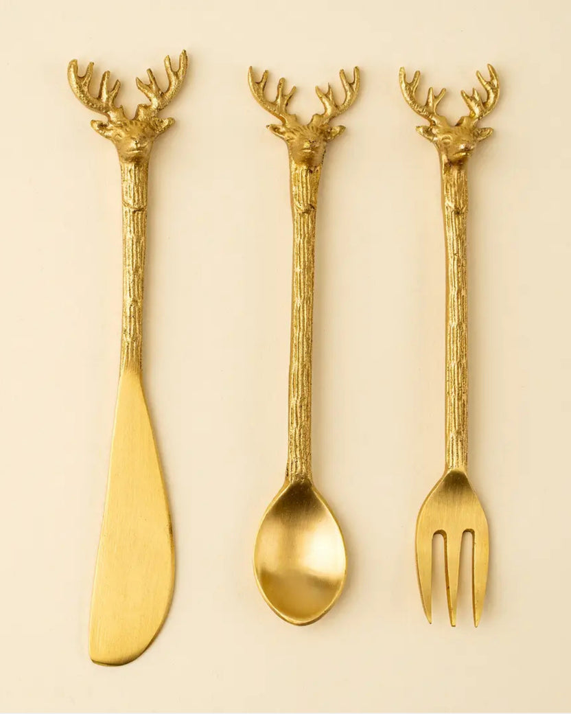 Three gold-colored cheese tools with stag head handles: a spreader, spoon, and fork.