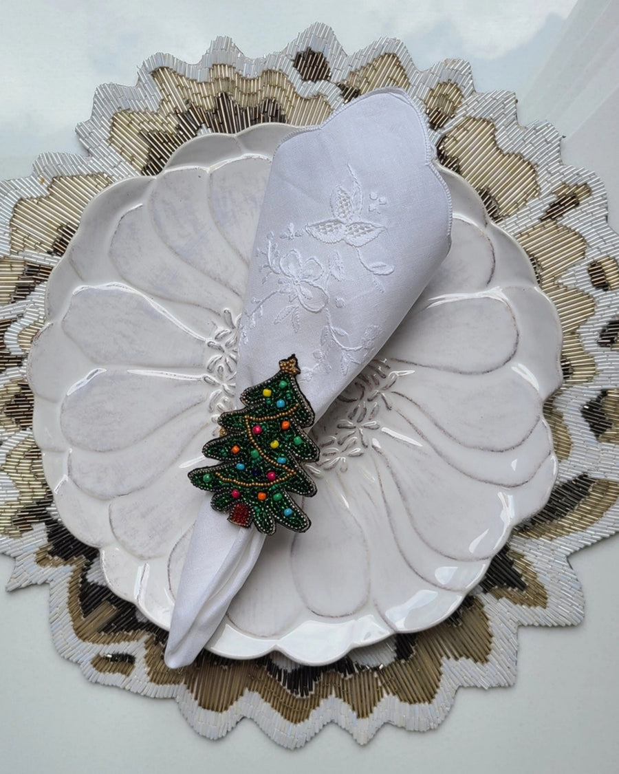Christmas tree napkin ring securing a folded white napkin on a decorative plate