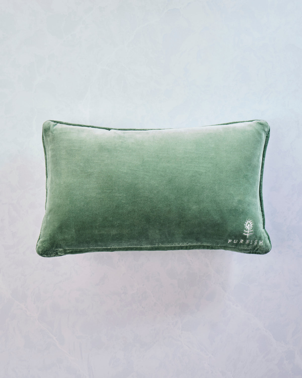 Back of a green rectangular needlepoint pillow with a Furbish logo embroidered in the lower-right corner.